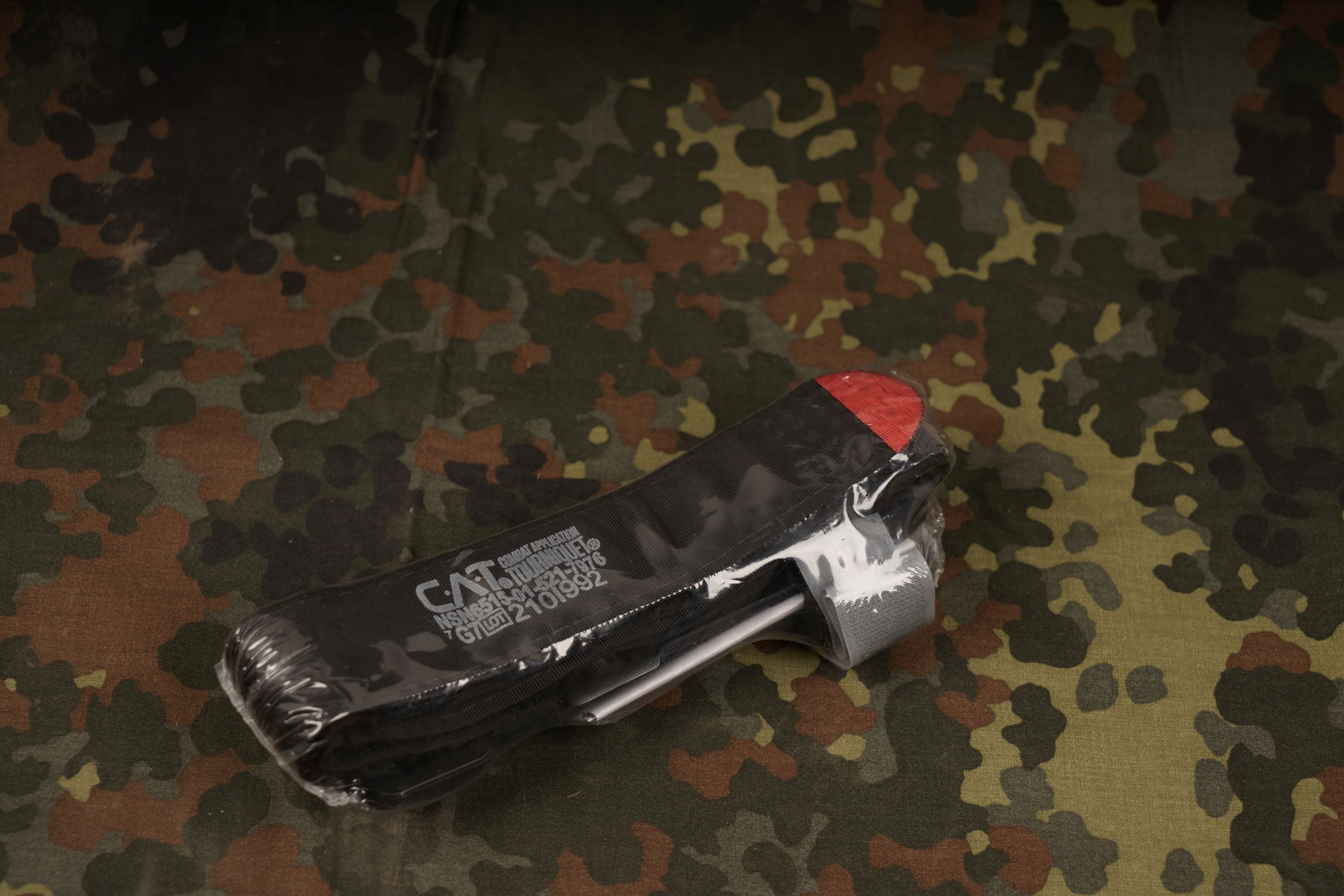 Frontalbild eines Combat Application Tourniquet "CAT 7", einer Hemostatischen Binde vor einem Flecktarn Hintergrund